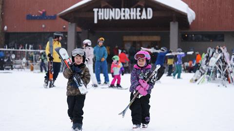 Two kids carrying their skis.