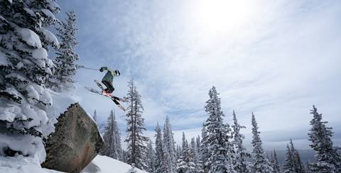 skier jumping off a rock in the sunshine